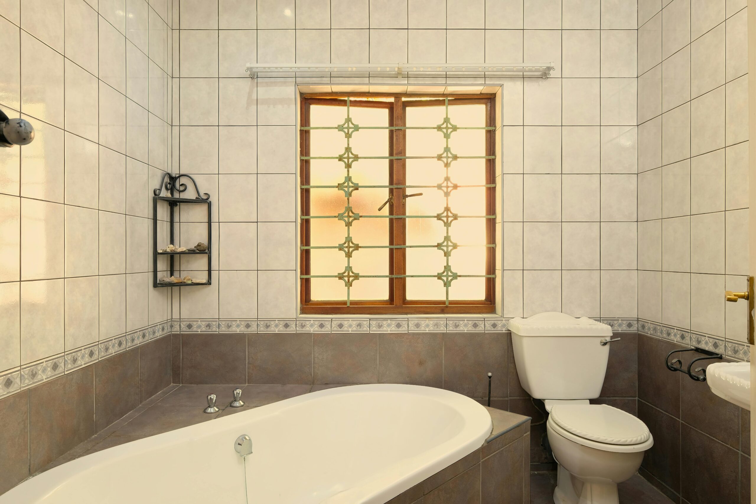 Elegant bathroom featuring a bathtub, toilet, and window with tiled walls.